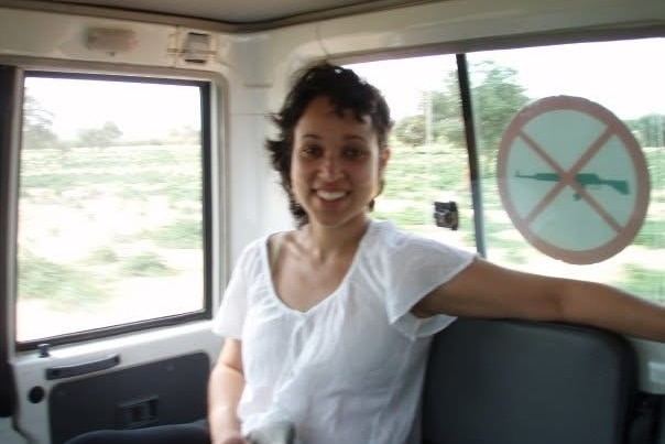 A young woman wearing a white top smiles as she sits inside a vehicle.