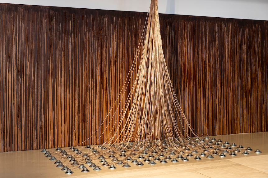 A brown canvas with many long golden cords connecting to silver circles on the ground.