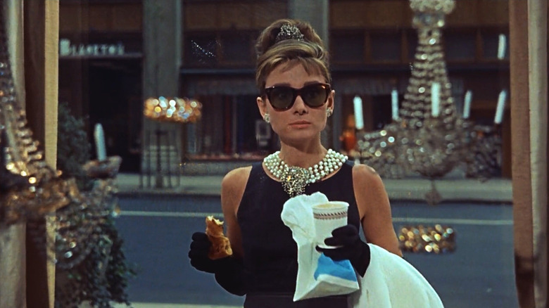 Holly with some food, in shade, looking through a window in Breakfast at Tiffany's