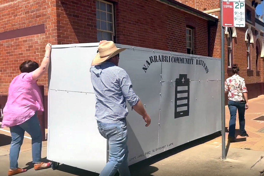 Three people pushing a large grey box that says Narrabri community battery 