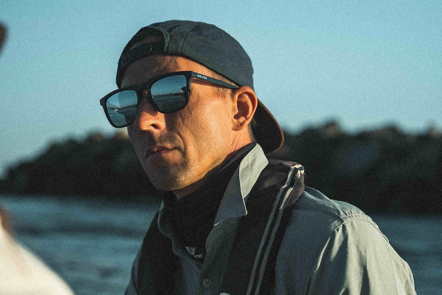 A man looks up and into the distance as he sits on the edge of a boat at sea.