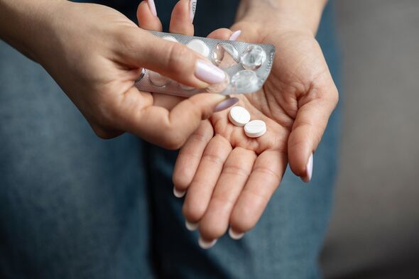 Close-up of female hands taking pills from blister pack with white round scored tablets, concept of pharmaceutical treatment