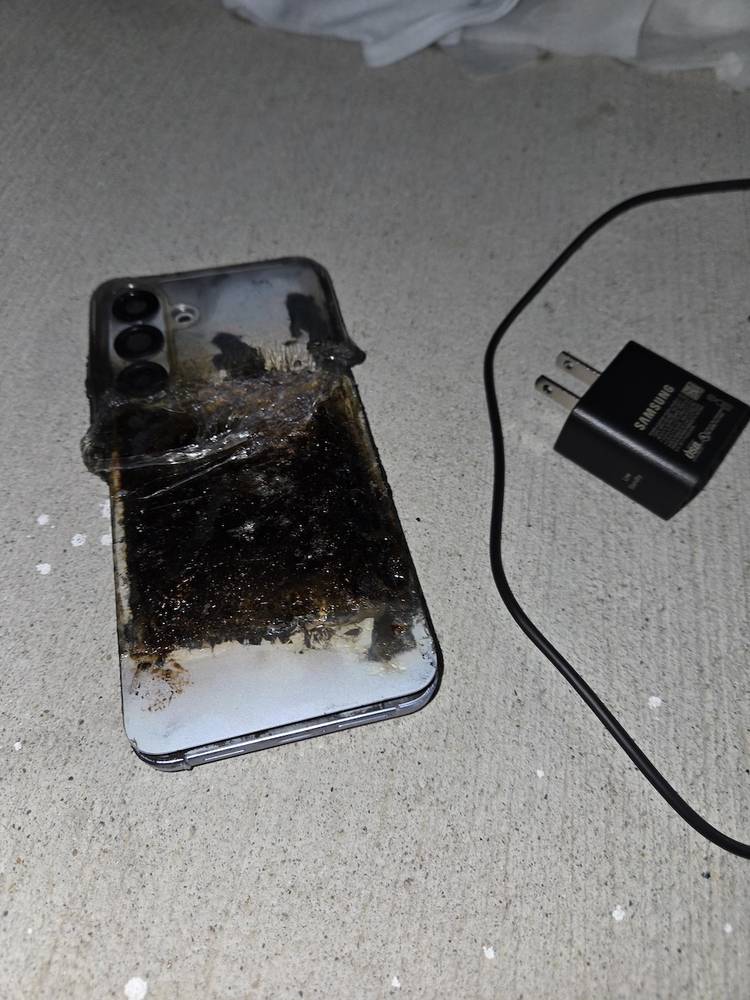 Burnt silver Galaxy S25+ phone on carpet beside black Samsung charger