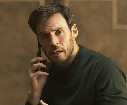 Sam Claflin as Laz holding a cell phone to his right ear while looking concerned in Harlan Coben's Lazarus