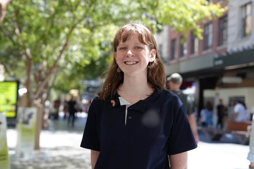 A teenage girl with long, straight hair, wearing a dark polo shirt, smiles.