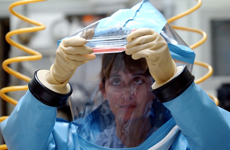 A researcher in PPE closely examines a sample material inside a bio safety level 4 lab.
