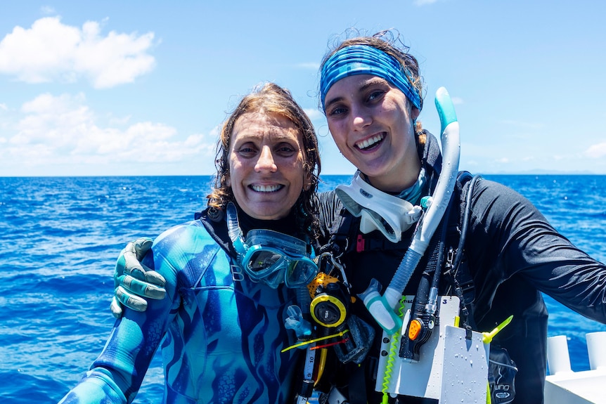 mother and daughter hugging on a boat in scuba gear.