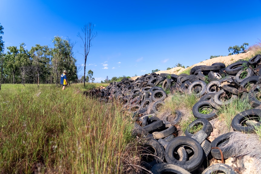 A wide shot of a large tyre dump with a man in the foreground.