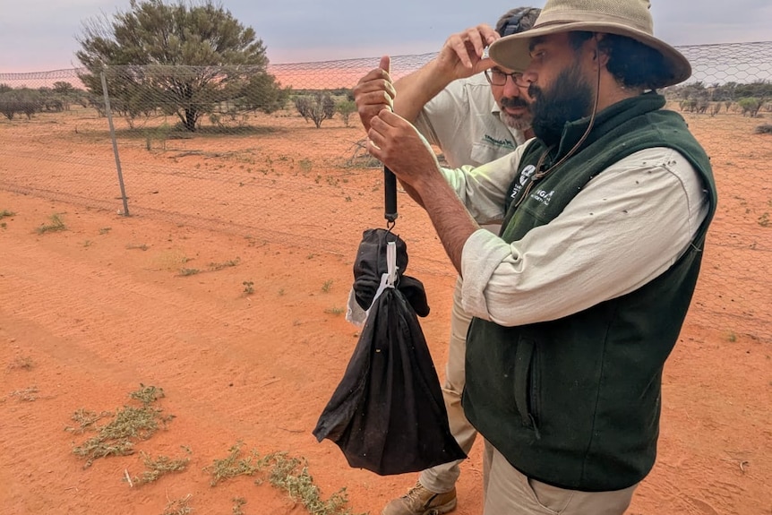 Two men talking to each other holding a bag.