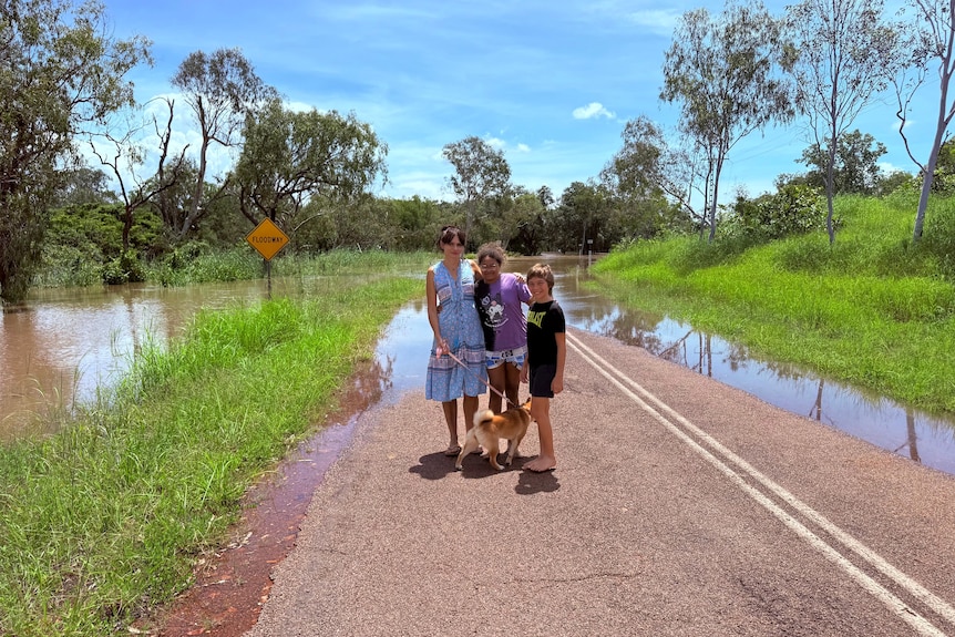 A man, woman and two children with a dog standing in front of a flooded road. 