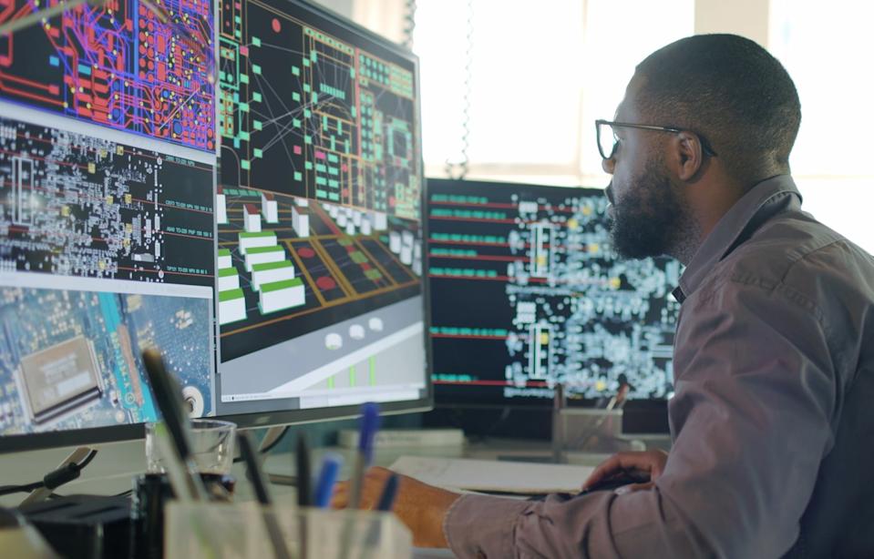 A software engineer sits at a large computer screen. A secondary, smaller screen is to his right. 