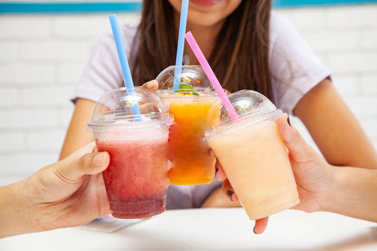 A group of three teens cheers their sugary iced drinks.