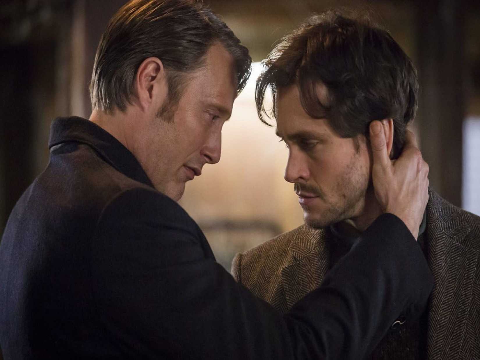 Mads Mikkelsen as Hannibal Lecter leans in to press a hand to the back of Will Graham's (portrayed by Hugh Dancy) head. Image from NBC Hannibal by Bryan Fuller.