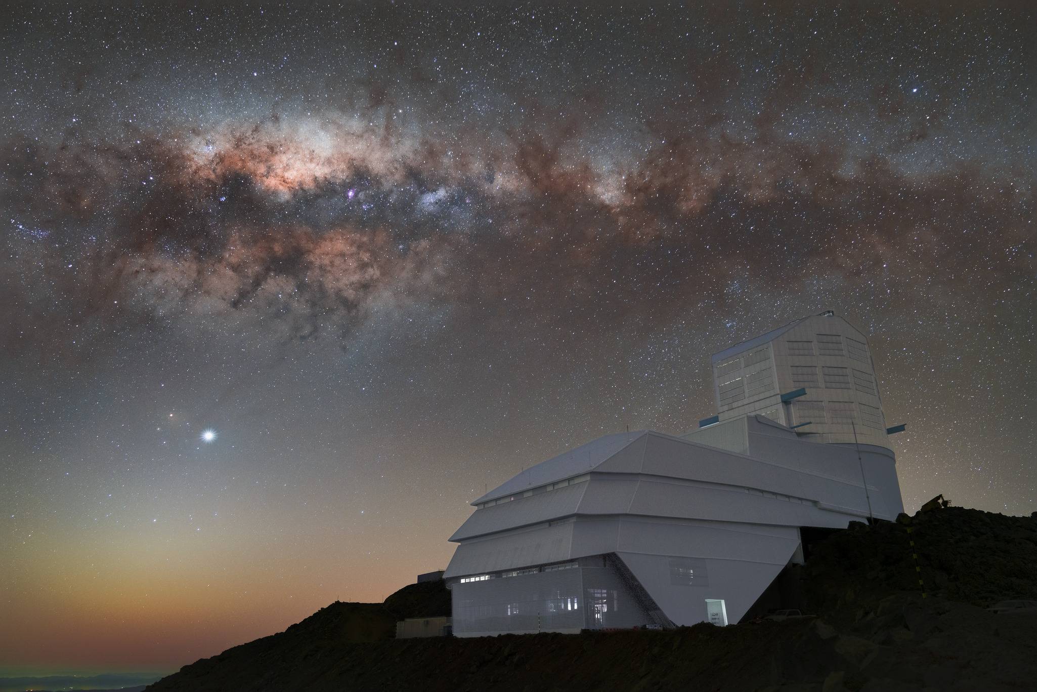 A series of red and purple clouds over a white building sitting on a cliffside