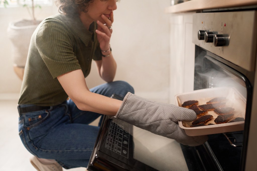 A woman taking a tray of burnt food out of an oven.
