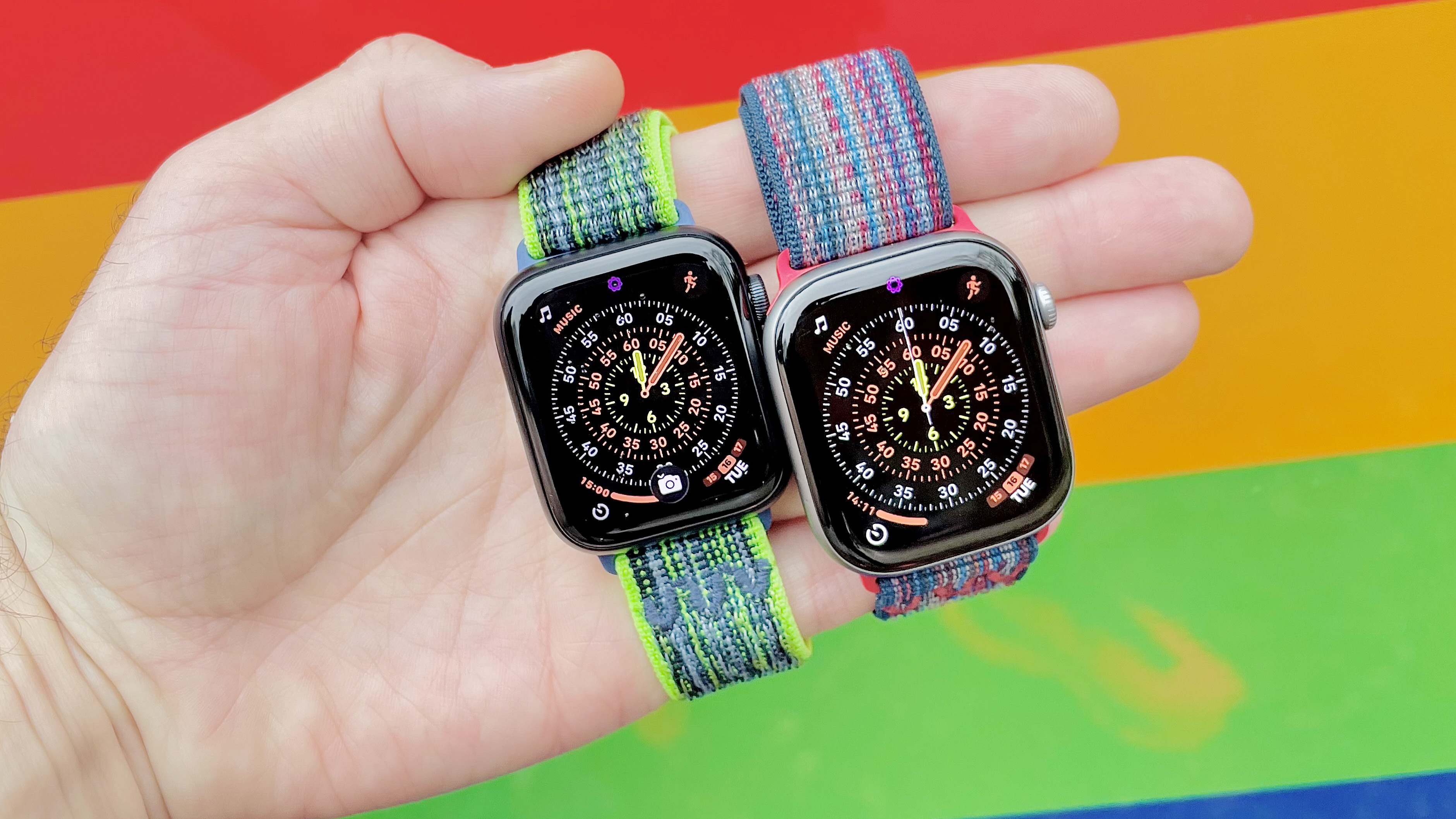 Close-up of the Apple Watch SE 3 and Apple Watch Series 11 in a user's hand with a colorful, out-of-focus background