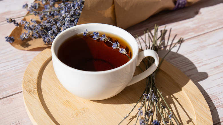 A cup of lavender tea on a wooden saucer surrounded by lavender sprigs