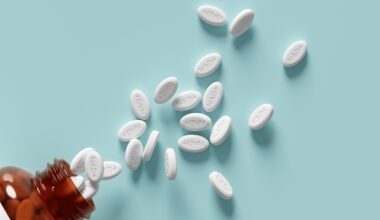 White pills labelled NAD+ spilling out of a brown pill bottle onto a light blue surface.
