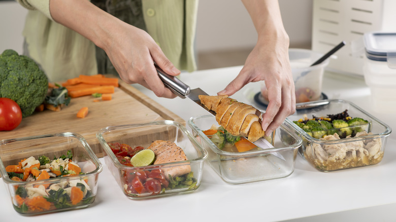 Row of glass dishes with different balanced meals being placed in them by a person