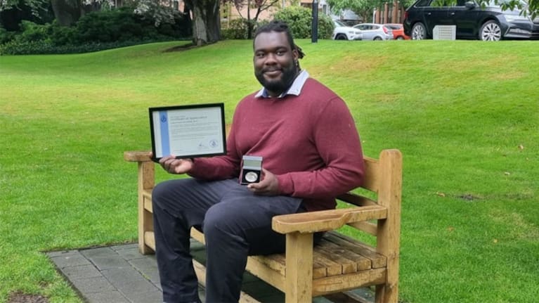 Samson Aruwa on the seat dedicated to Sophia Crestani in Dunedin. (Source: RNZ / Tess Brunton)