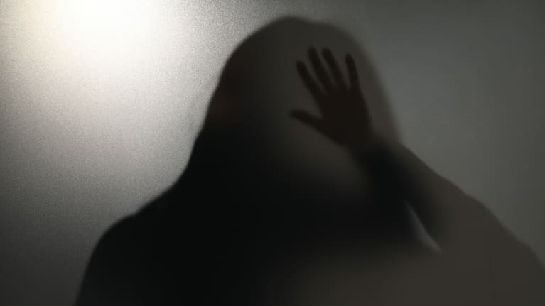Silhouette of ghost behind glass against light grey background stock photo.