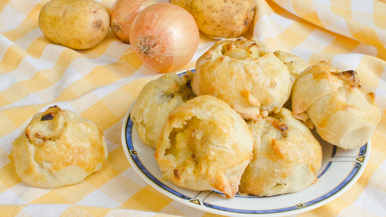 plate of round potato knishes with potatoes and onions in the background on a striped yellow tablecloth