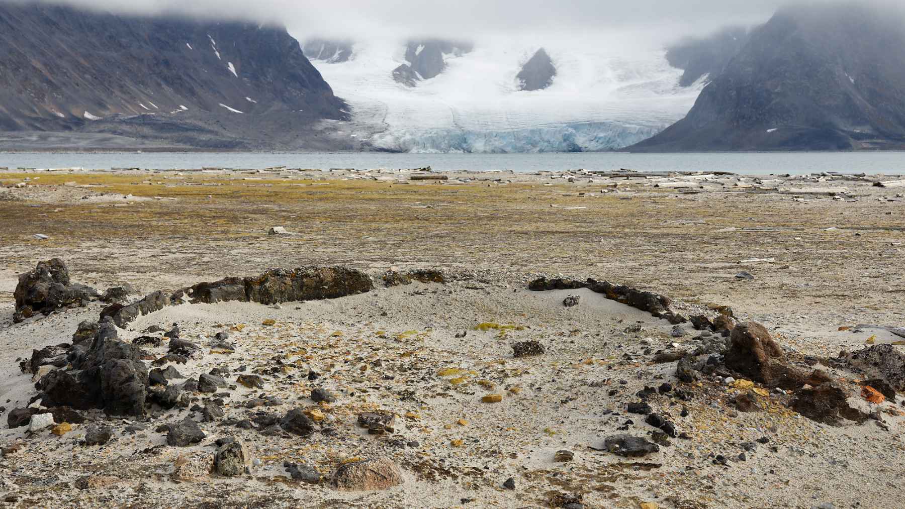 Remains of a 17th-century blubber oven at Smeerenburg with glacier and Arctic mountains in Svalbard.