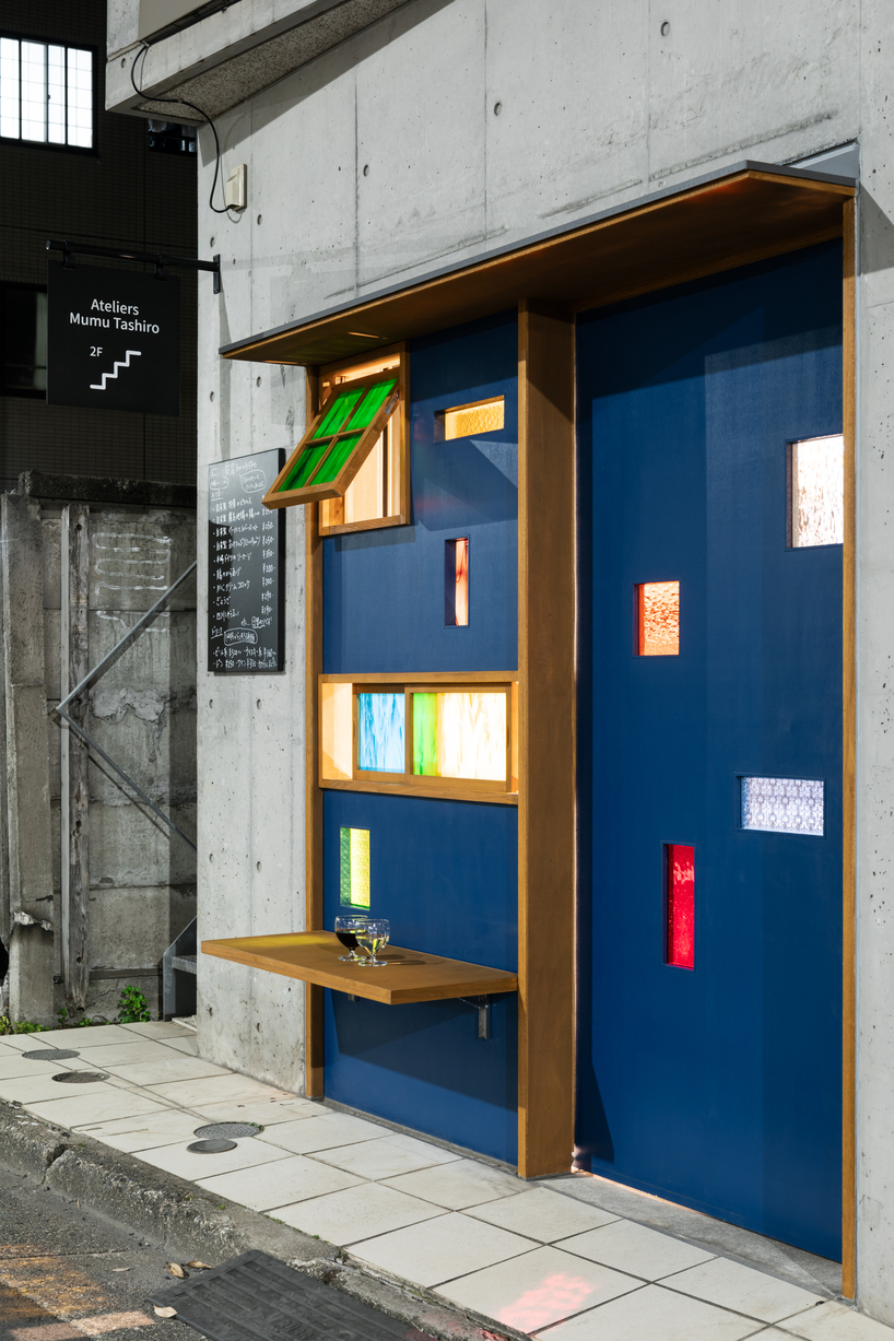 colored glass apertures reveal lively tokyo bar through bright blue entrance