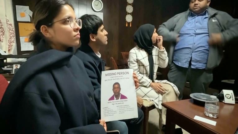 This image made from video provided by WKBW.COM shows a family friend holding a missing person flyer for Nurul Amin Shah Alam, while sitting with other family friends including Khaleda Shah, second from right, and MD Karim, far right.