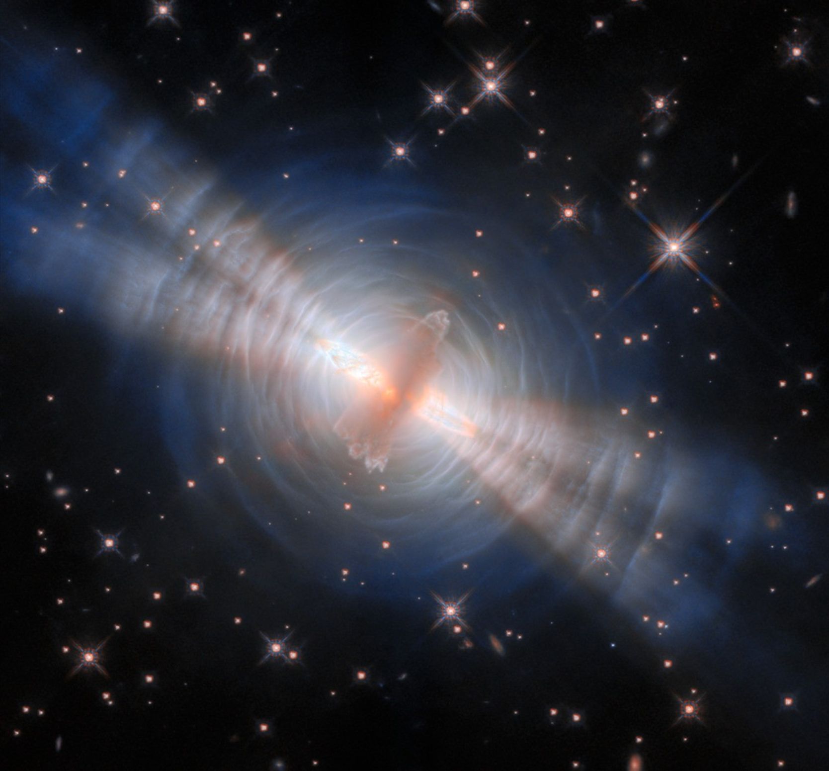 A beautiful image of space with sparkling stars in the background. There's a bright hazy structure in the center surrounded by a shell of blue-ish dust and with four streaks of light coming out of it.
