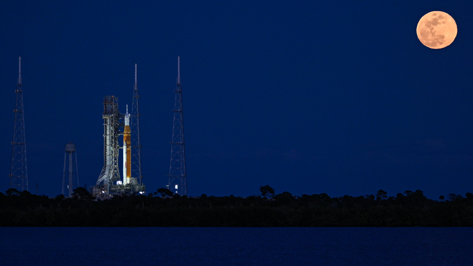 A rocket on the launch pad at night with the full moon in the background
