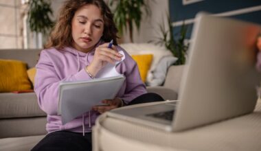 Student at home studying from notes while sitting in front of a laptop.