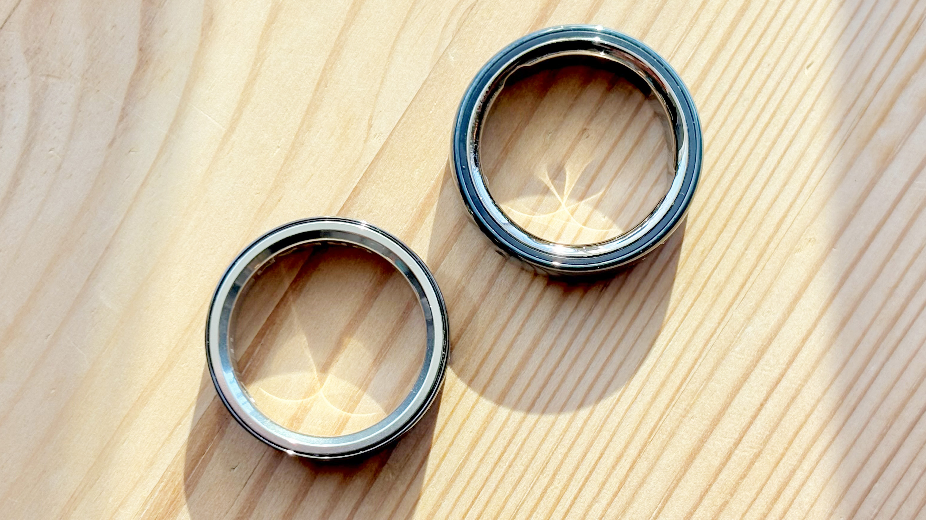 Close-up of the Dreame Smart Ring next to the Oura Ring 4 Ceramic on a wood table