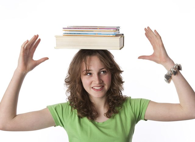 Teenage girl is carrying text books on her head at white background