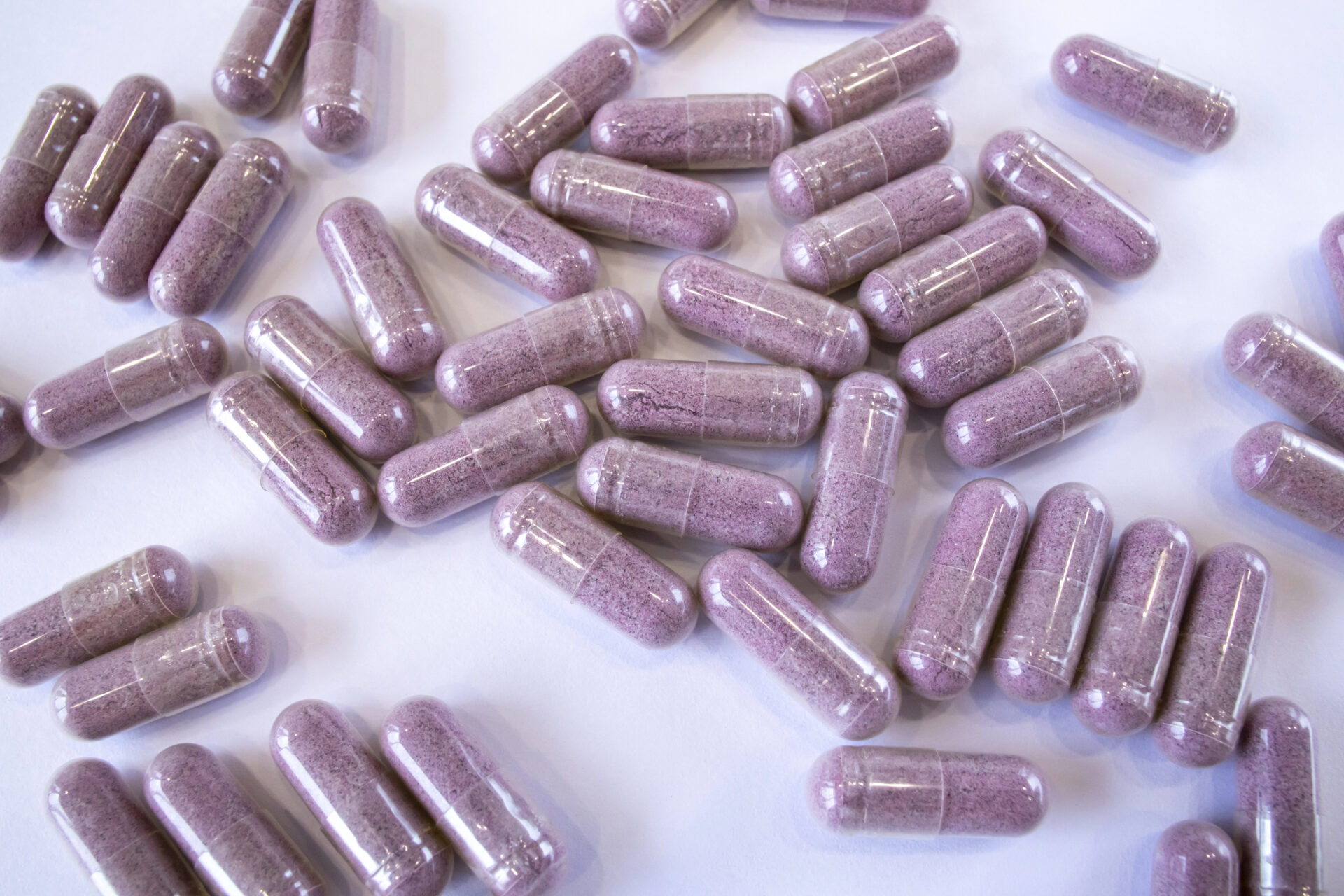 Pink capsules with additives on a white background. Pills and medicines. Tart cherry additives, vitamins, minerals, plant extracts and other beneficial substances. 