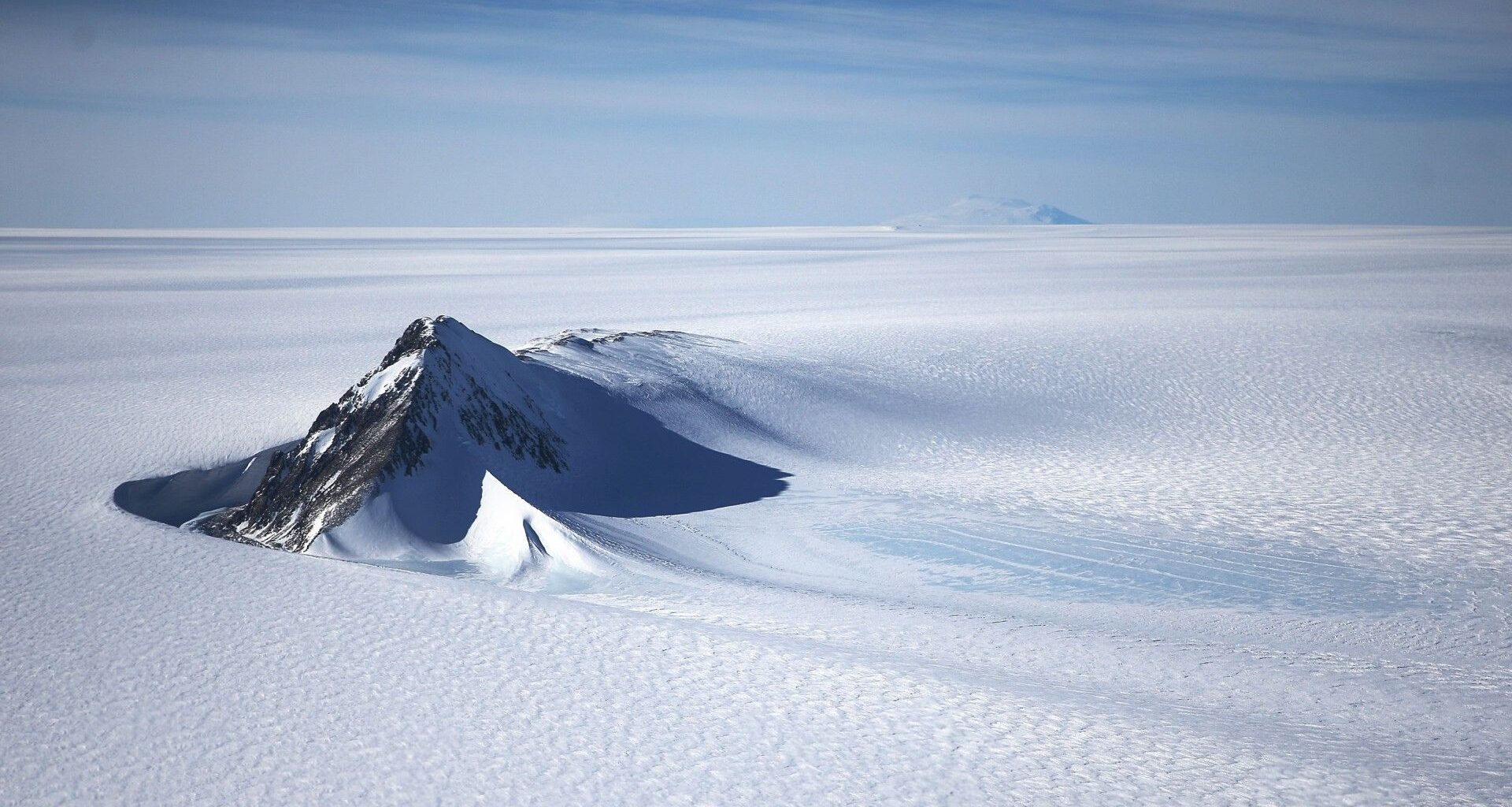 the tip of a rocky mountain rises up out of a snowy expanse