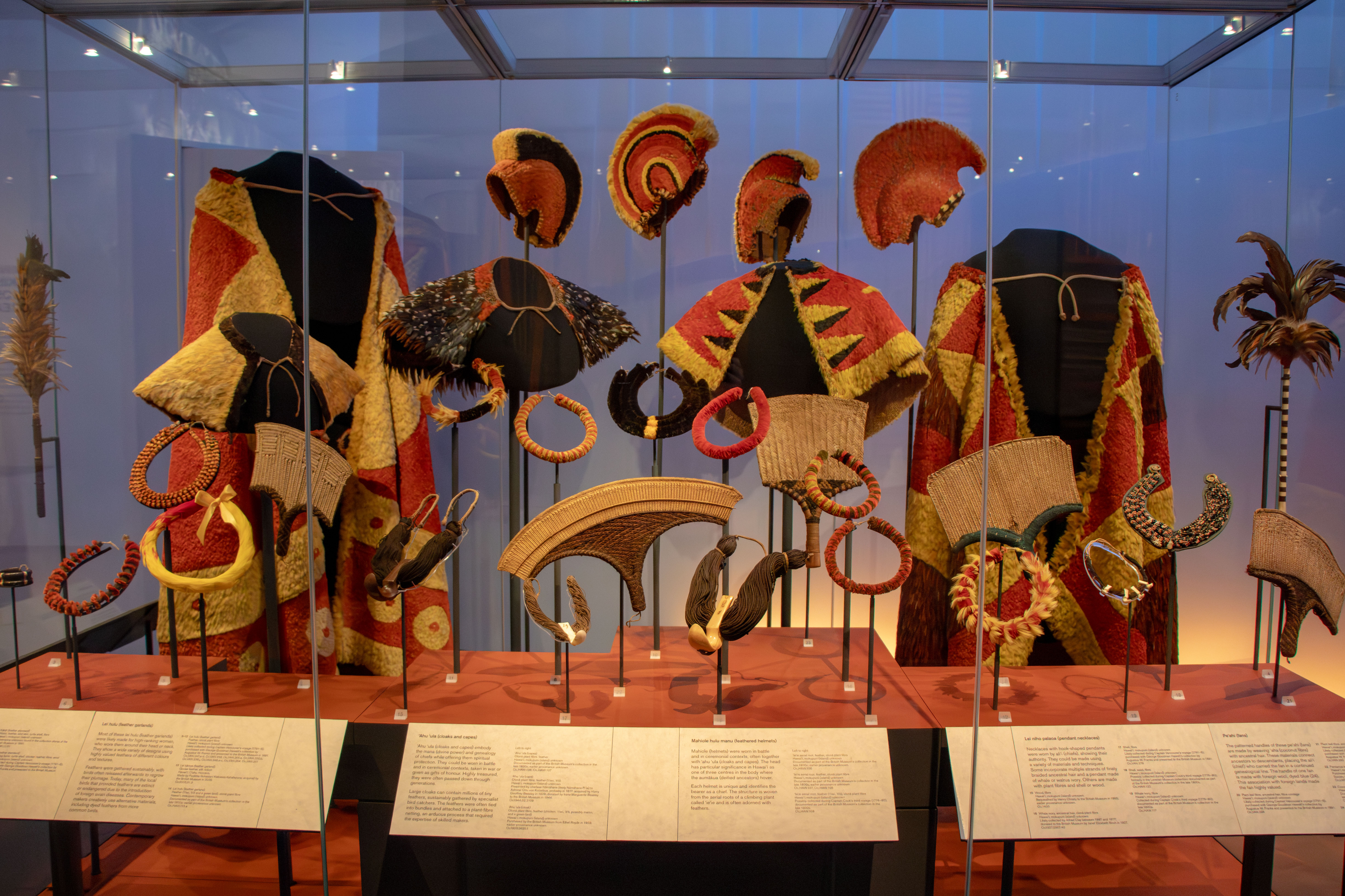 Featherwork ornaments, including capes, helmets, and necklaces, on display.