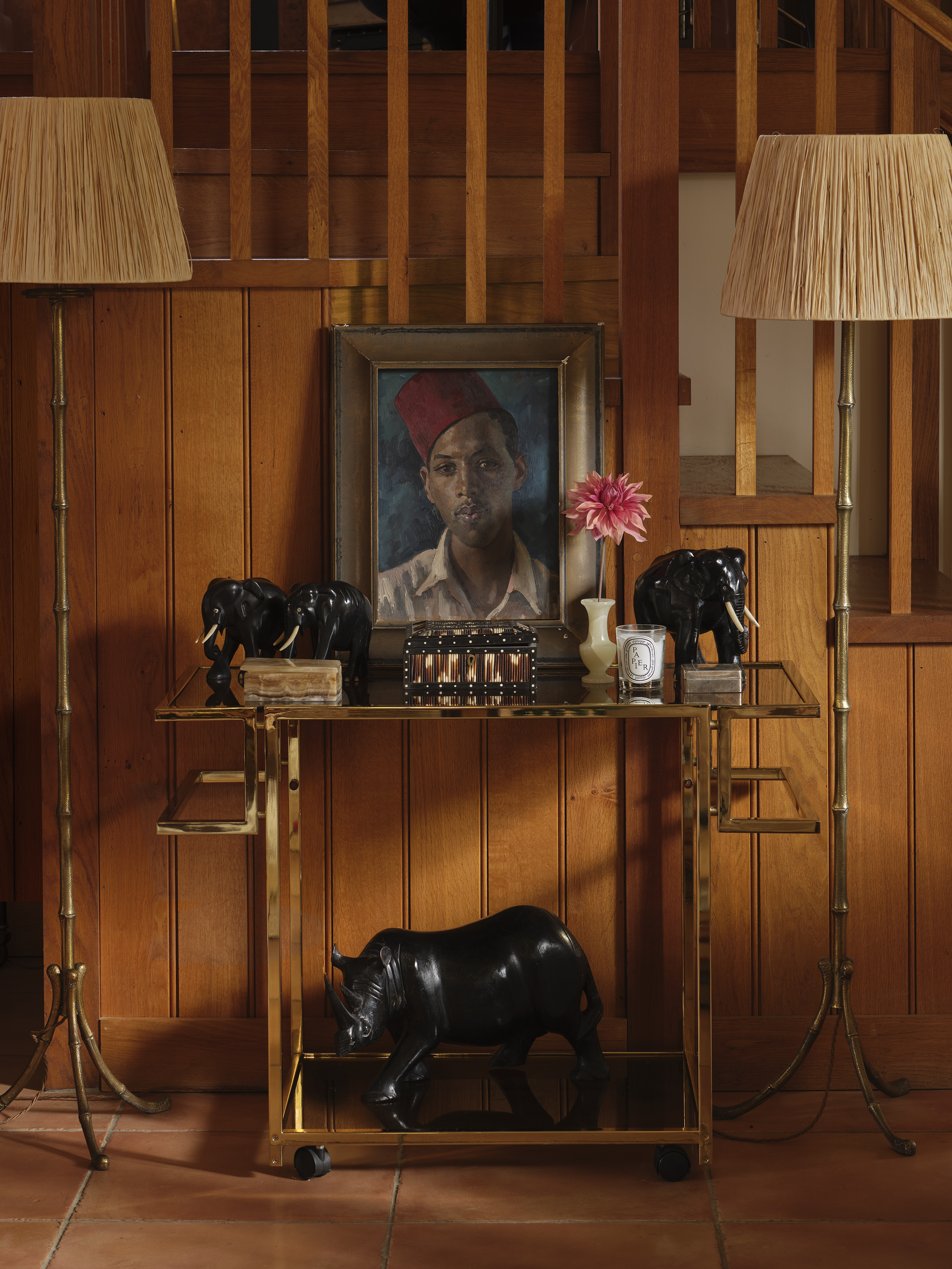 An entryway decorated with a painting, a golden bar cart, and two lamps.