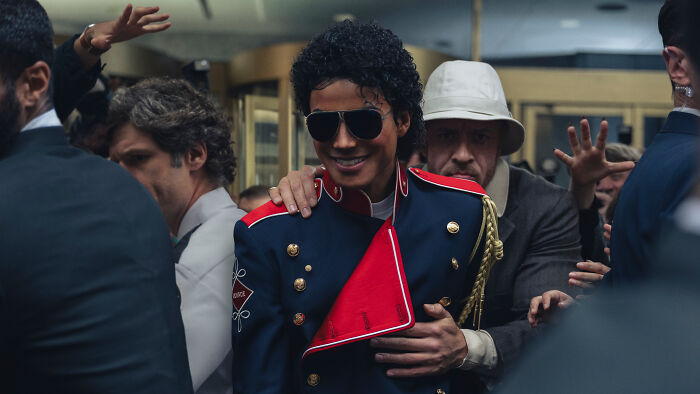 Actor portraying Michael Jackson in the Michael movie cast, dressed in a red and blue military-style jacket with sunglasses.