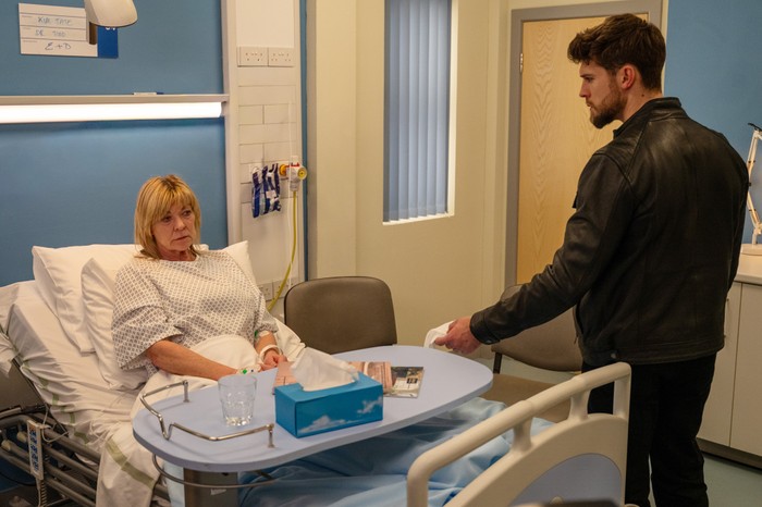 Joe stands over Kim's hospital bed in a scene from Emmerdale