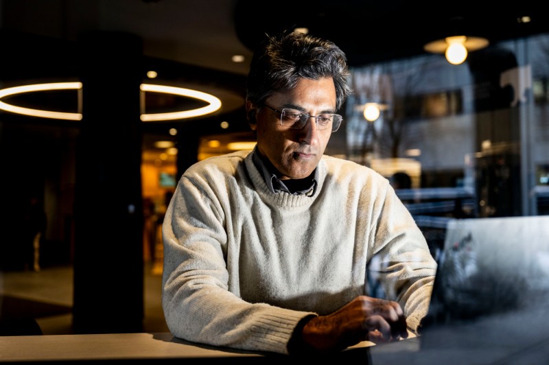 Kiran Vanaja, in a white sweater, types at a laptop on a desk.