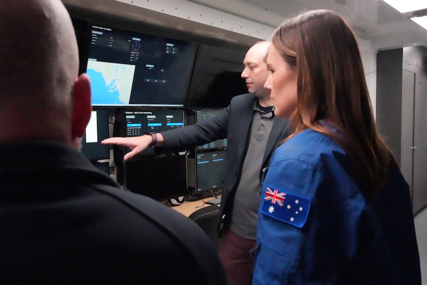 Three people look at space communications technology.