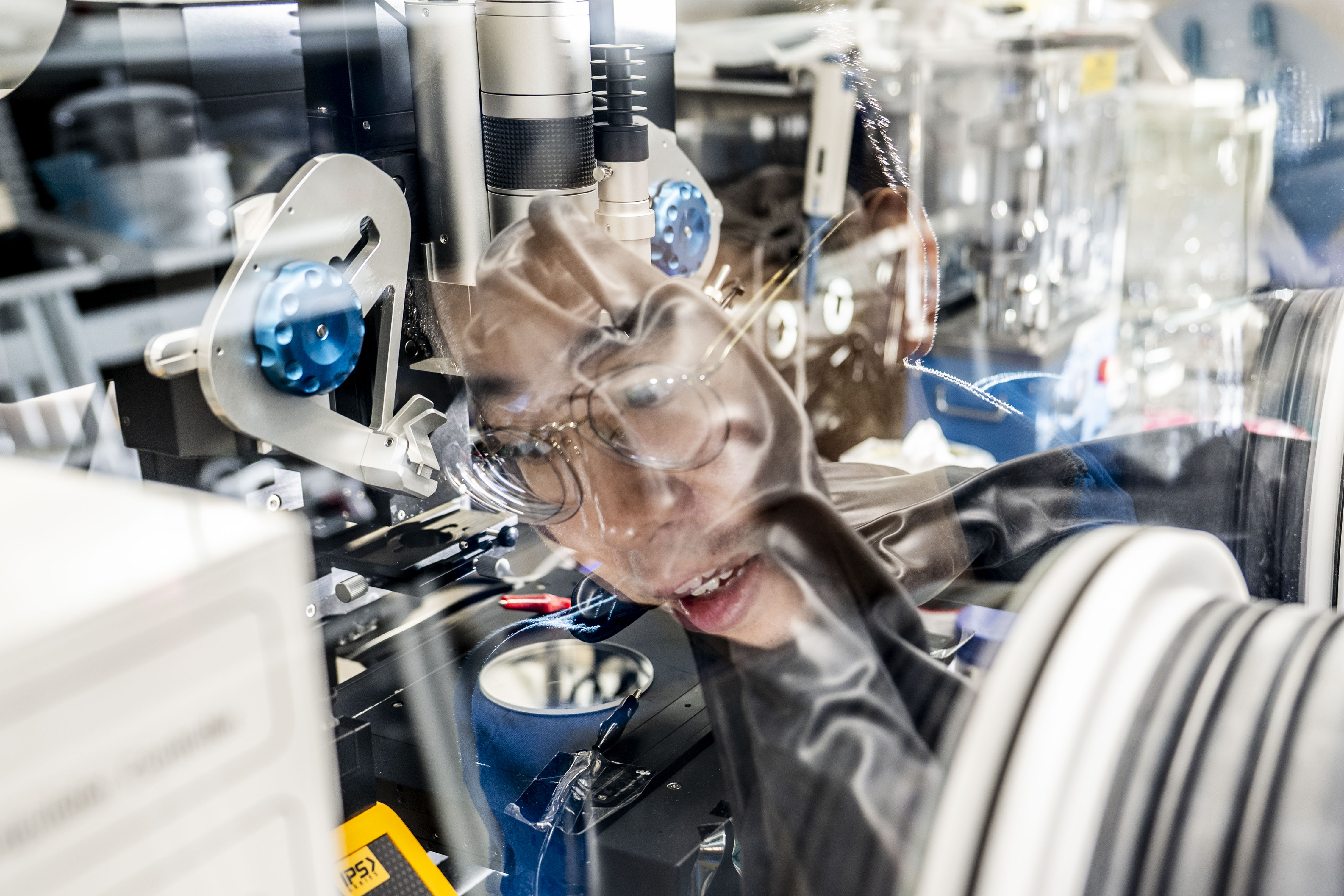 A researcher peers into a microscope while working with lab equipment during battery research.