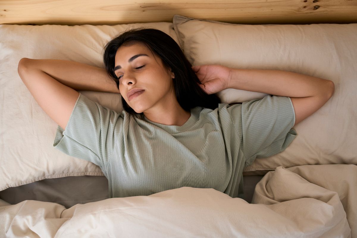  Peaceful sleep: young woman resting in bed with arms behind her head, enjoying a moment of tranquility
