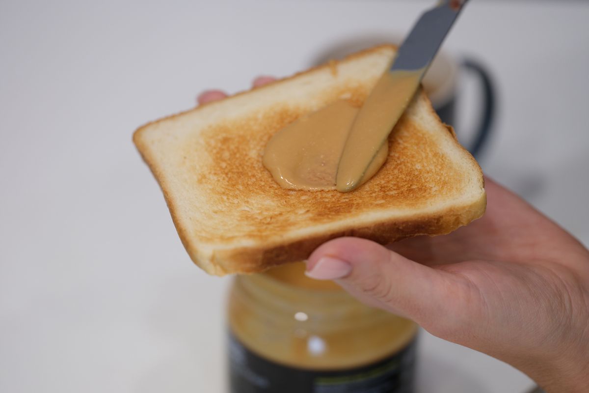 Woman spreads peanut butter on toast with knife. Benefits and harms of peanut butter sandwiches in the morning concept