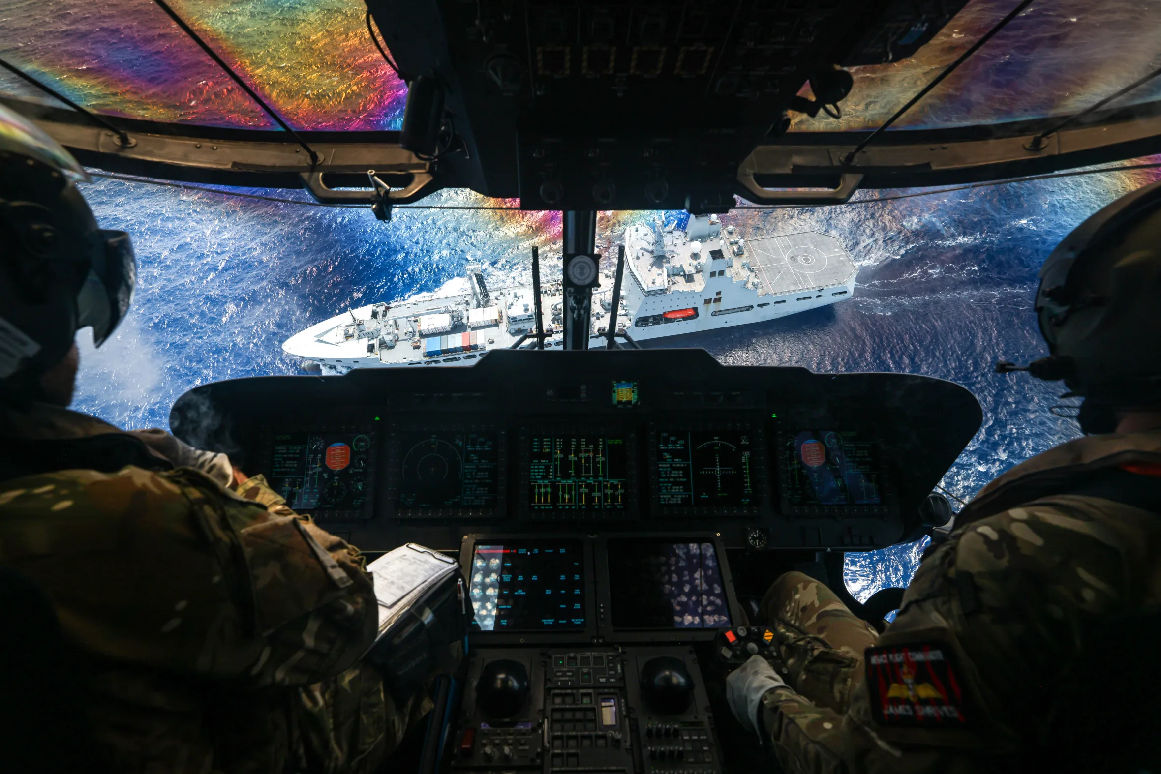 View from a helicopter cockpit looking down at a large white ship in blue water.