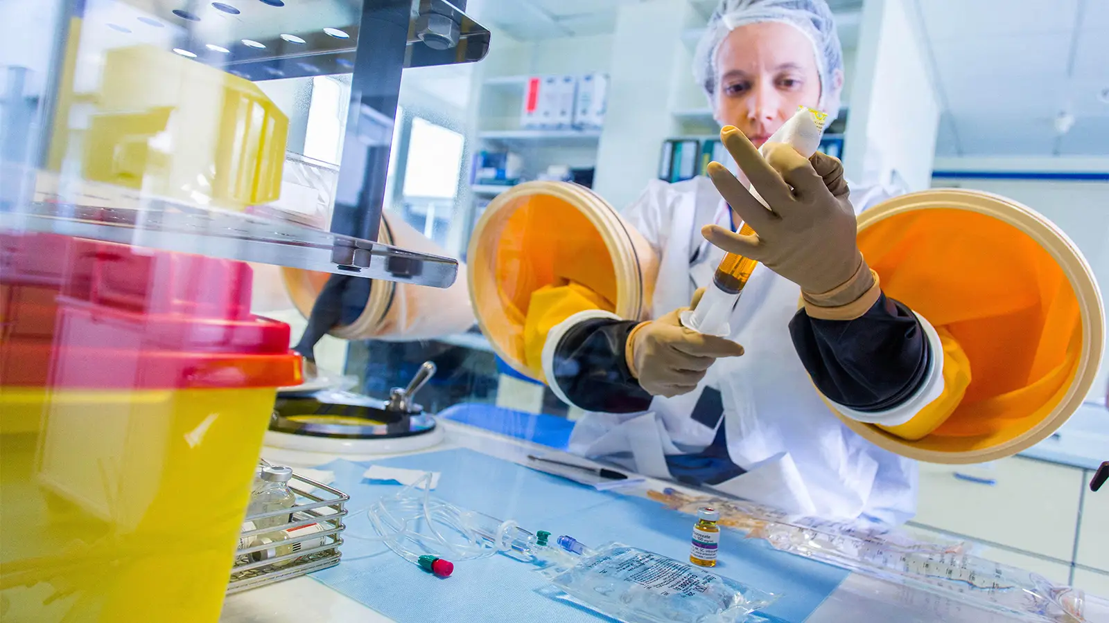 A photo of a female healthcare worker preparing chemotherapy treatments under a glove box.