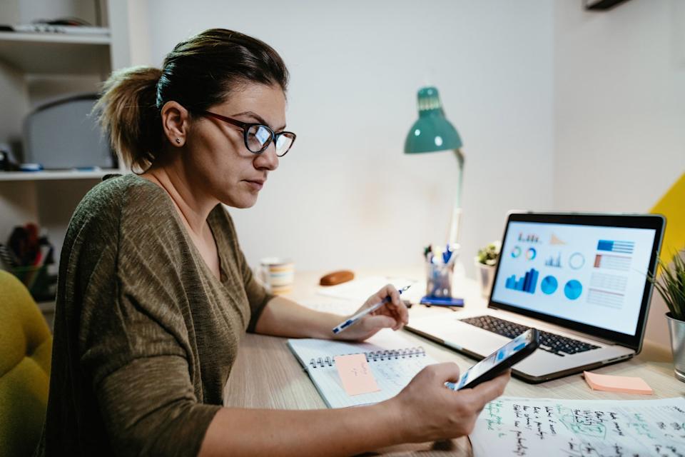 A person sitting at a desk in front of a laptop, reviewing paperwork.