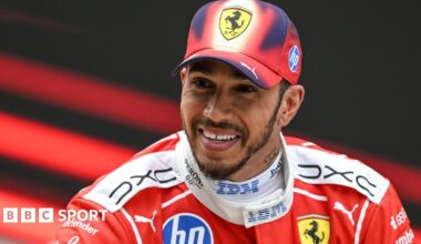 A smiling Lewis Hamilton wearing a Ferrari cap and race overall after he finished third in the Chinese Grand Prix