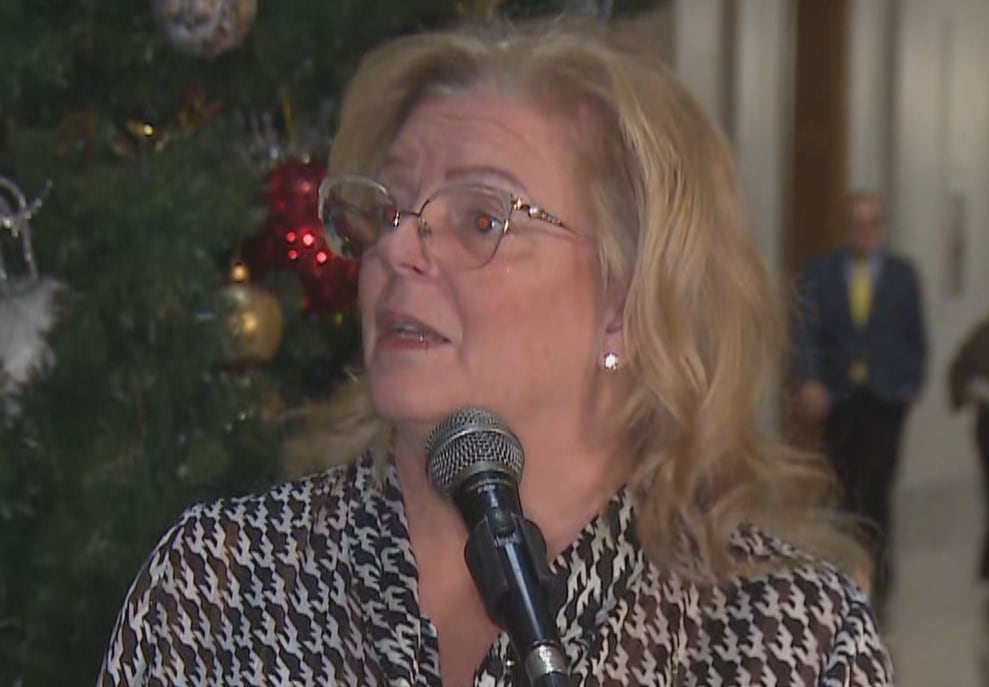 A woman with glasses speaks into a microphone in the rotunda of a legislative building. 